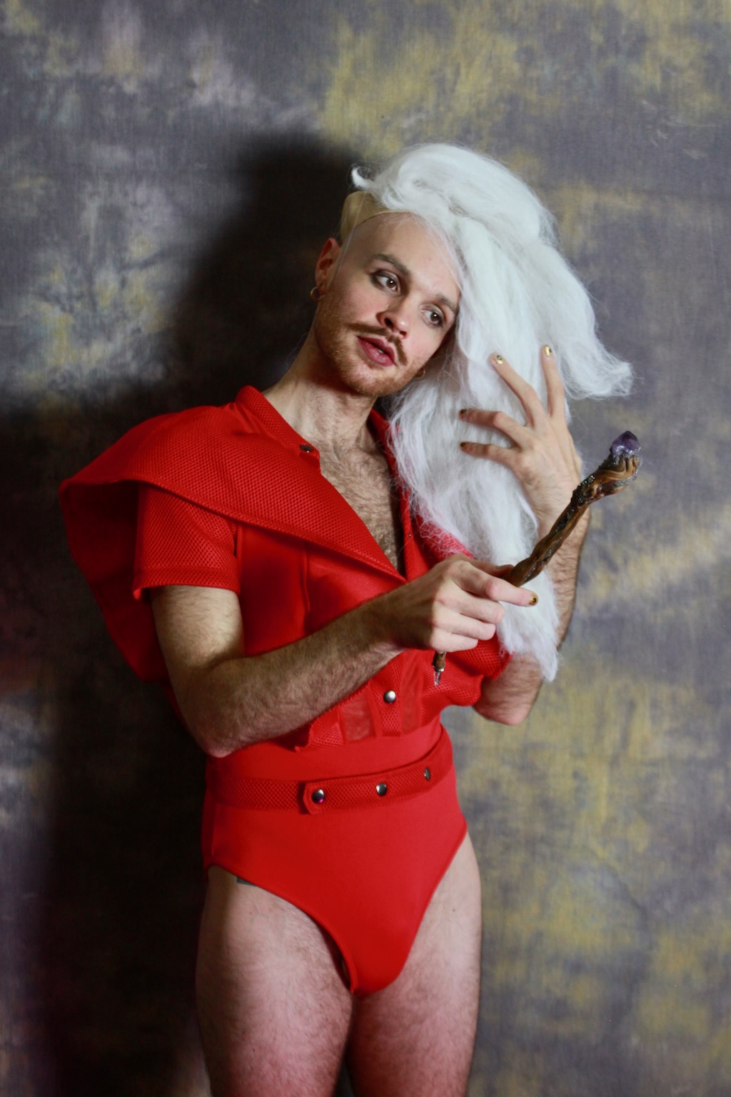Person wearing red jumpsuit and wizard hair with a wand
