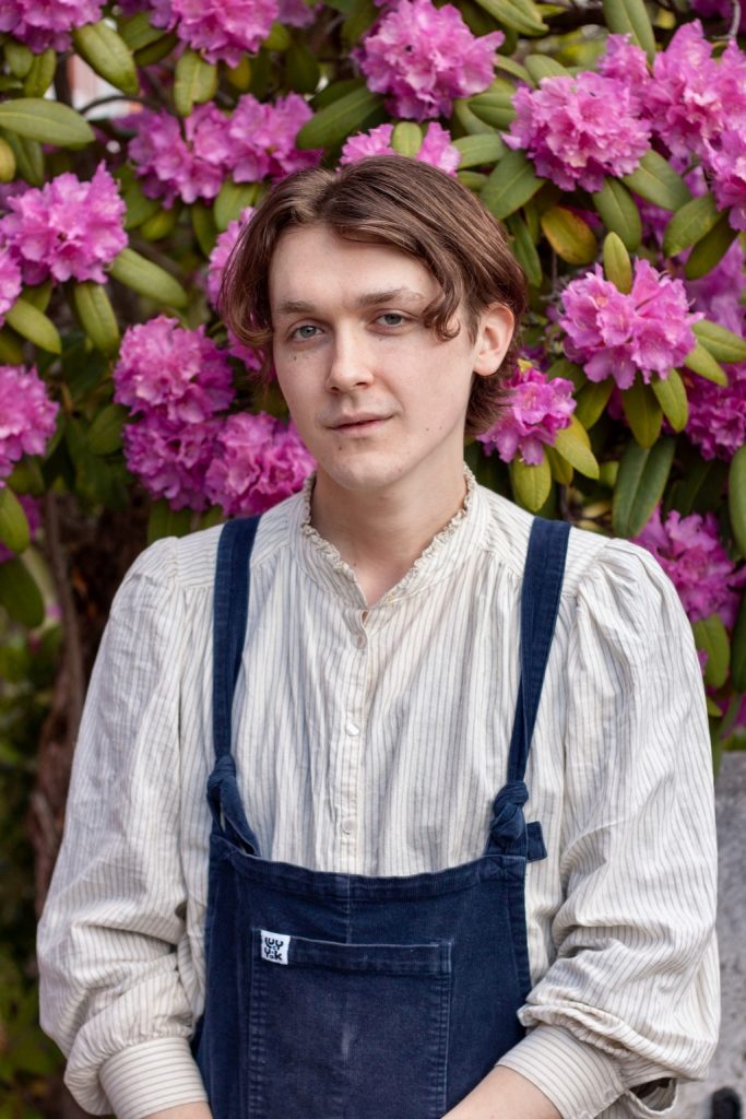 Person wearing dungarees in front of pink blossom